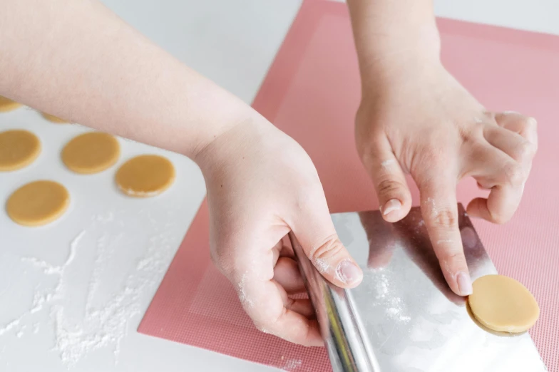 a person cutting a cookie with a pair of scissors, a silk screen, trending on pexels, covered with pink marzipan, tabletop, children's, silicone skin