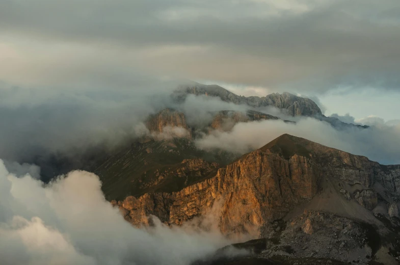 a mountain with fog floating over it and a sky full of clouds