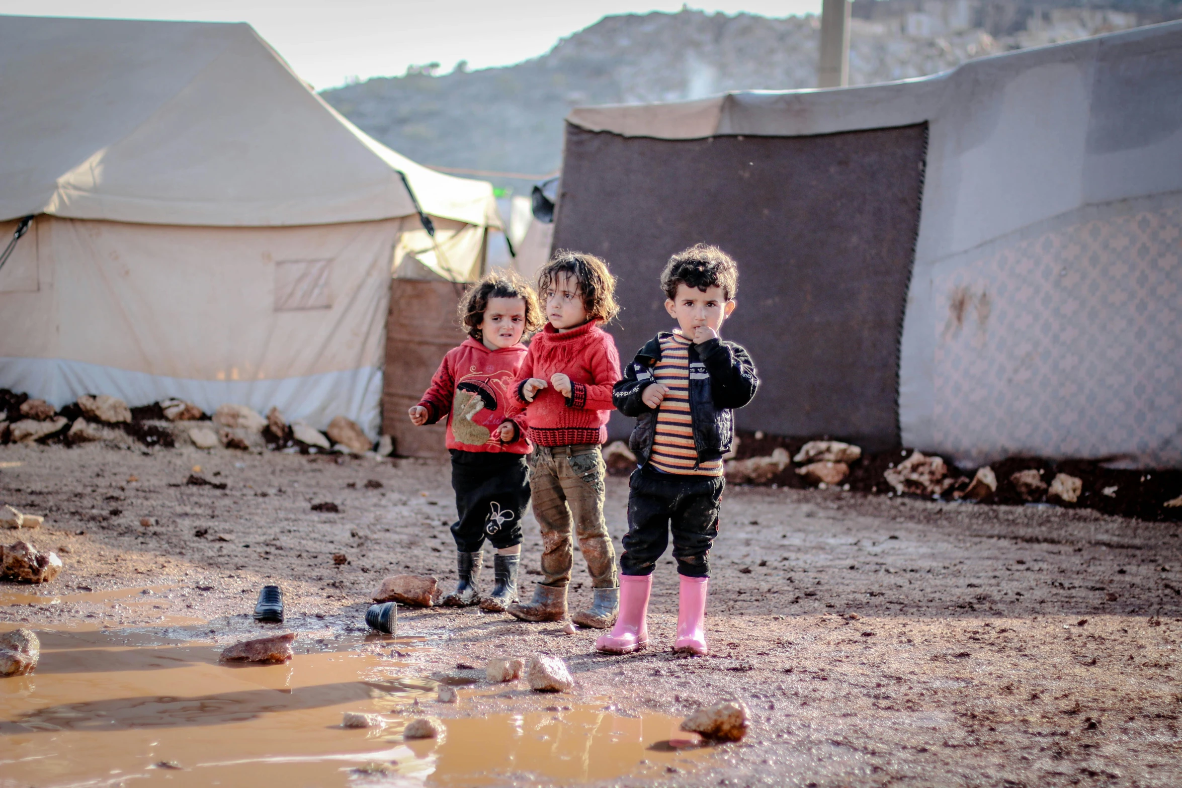 a couple of kids that are standing in the dirt, by Lucia Peka, trending on unsplash, hurufiyya, tent camp in foreground, damascus, poop, the three moiras