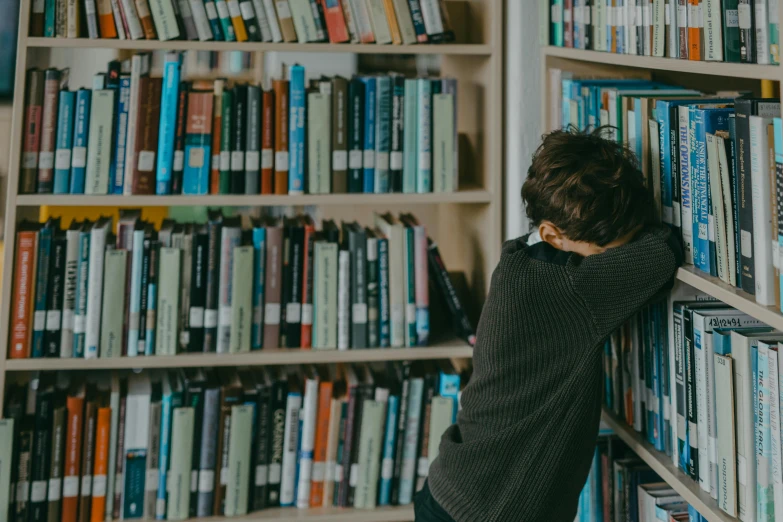 a person leaning against a bookshelf in a library, pexels contest winner, head bowed slightly, teenage boy, hunched over, an ahoge stands up on her head