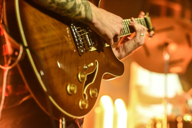 a close up of a person playing a guitar, a tattoo, gig, golden glow, heath clifford, live in concert