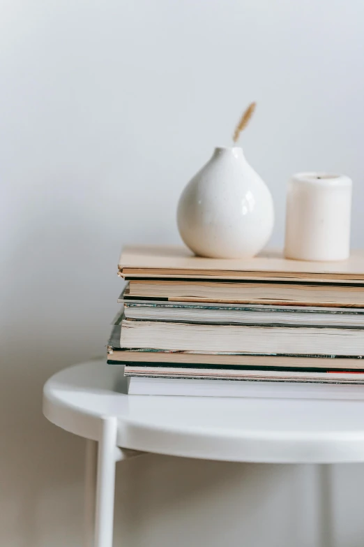 a stack of books sitting on top of a white table, a still life, trending on pexels, minimalism, white candles, beige color scheme, round-cropped, detailed product image