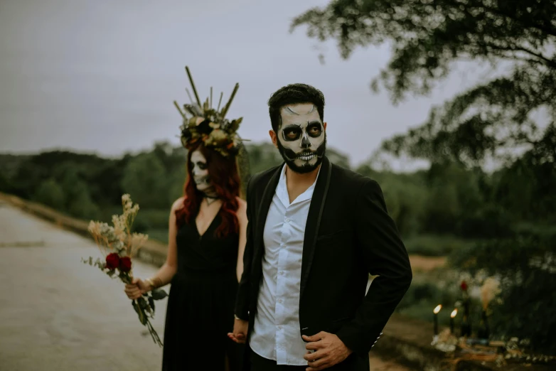 a man standing next to a woman in a black dress, by Alejandro Obregón, pexels contest winner, international gothic, skull face paint, promotional image, skull bones flowers, a person with a raccoon head