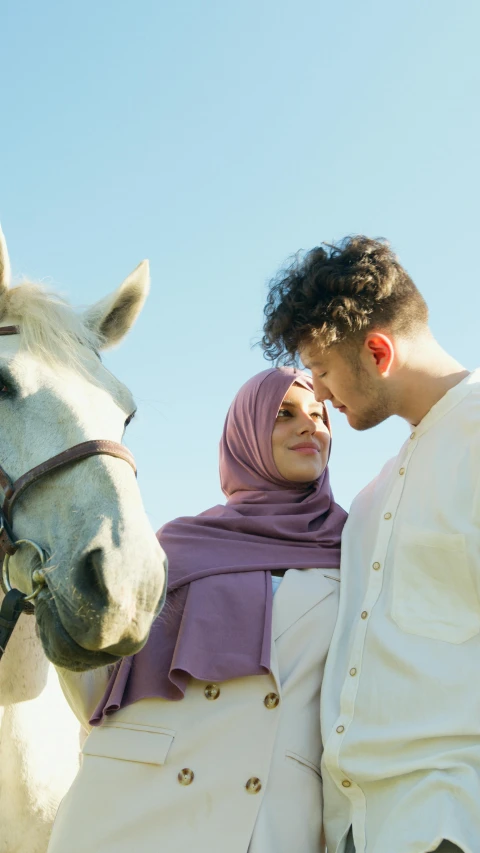 a man and woman standing next to a white horse, by Ismail Acar, trending on pexels, hurufiyya, hijab, square, flirting, pastel clothing