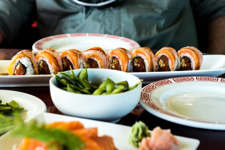 a person sitting at a table with plates of sushi, inspired by Maki Haku, unsplash, mingei, westside, seen from below, daily specials, amanda lilleston