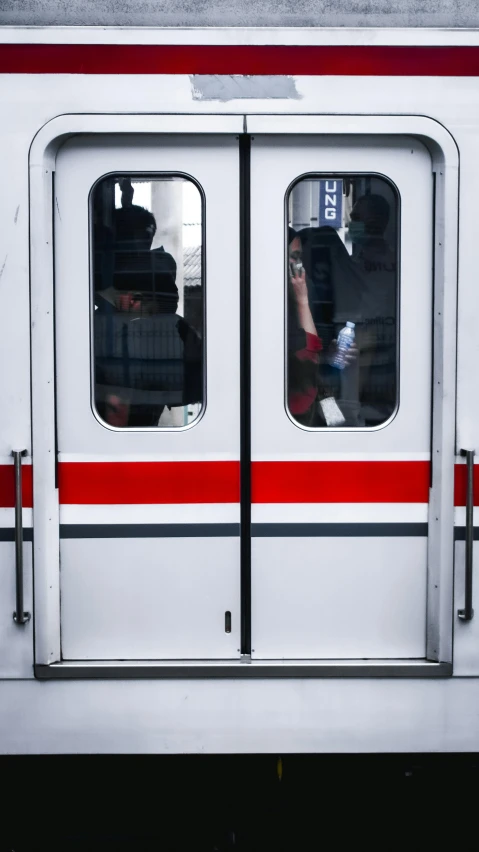 a red and white train traveling down train tracks, unsplash, tall door, low quality photo, 2 people, on a gray background