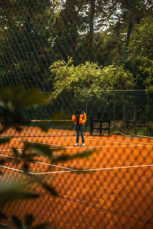 a man standing on a tennis court holding a racquet, by Jan Tengnagel, pexels contest winner, orange hoodie, spying, at the park, panoramic view of girl