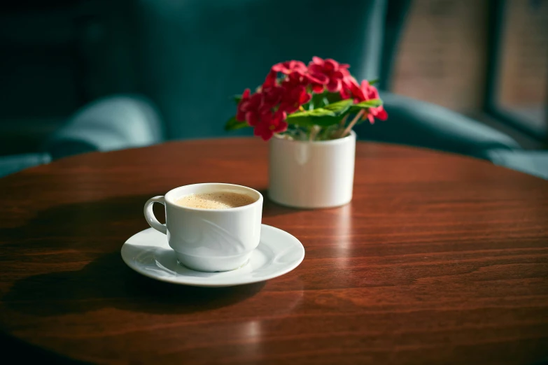 cup of coffee on the table with a vase of flowers in it