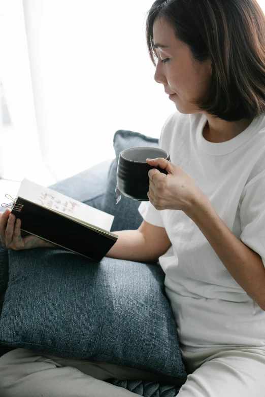 a woman sitting on a couch with a book and a cup of coffee, happening, abcdefghijklmnopqrstuvwxyz, multiple stories, old testament, gif