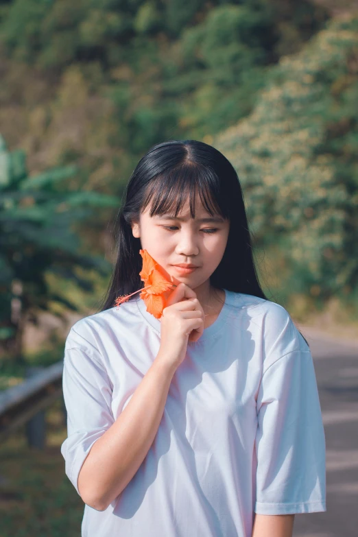 a woman holding an orange flower in front of her face, by Yan Liben, pexels contest winner, eating ice - cream, asian woman made from origami, 🚿🗝📝, wearing a light shirt