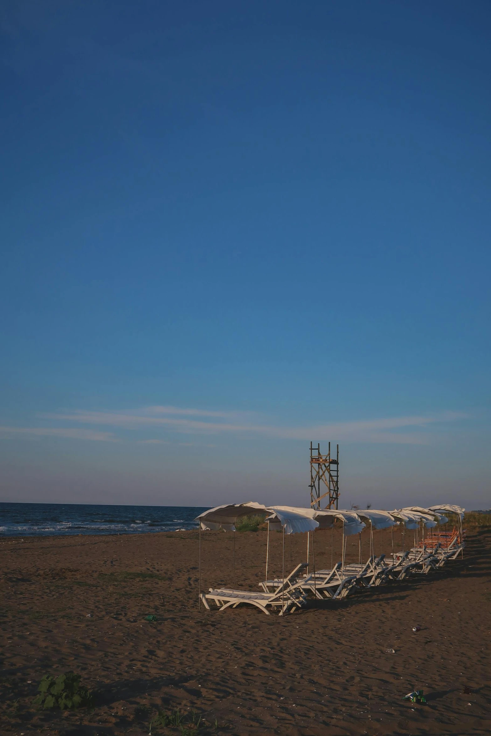 a row of beach chairs sitting on top of a sandy beach, a picture, by Carlo Martini, romanticism, black sea, 8 k ), desolate :: long shot, square