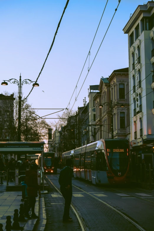 a train traveling down a city street next to tall buildings, by Niko Henrichon, pexels contest winner, happening, trams, late afternoon sun, instagram story, nice spring afternoon lighting