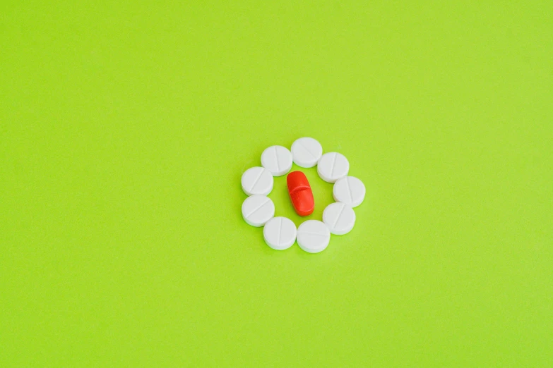 a red pill in a circle of white pills on a green background, pexels, an orange, hyperminimalist, small gadget, on a table