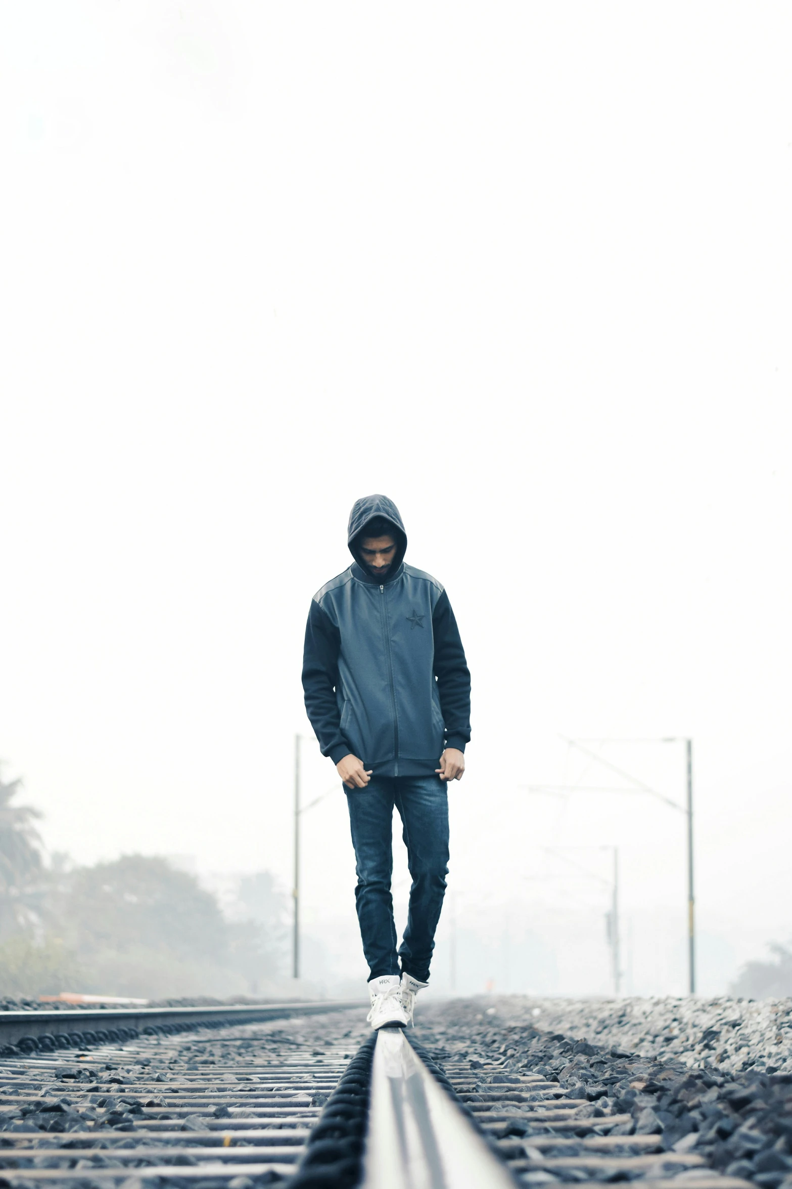 a man walking down a train track on a foggy day, a picture, trending on unsplash, minimalism, wearing jeans and a black hoodie, portrait full body, standing in a parking lot, wearing a blue hoodie