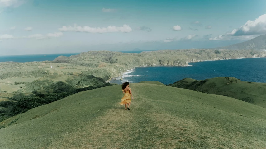 a woman standing on the top of a grass covered mountain