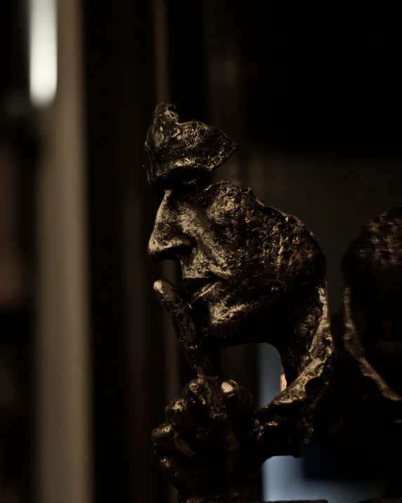 a statue of a man sitting on top of a table, a bronze sculpture, inspired by Alberto Giacometti, pexels contest winner, close - up profile face, on dark paper, small details, portrait of an ork