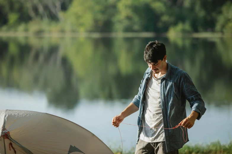 a man standing next to a tent next to a lake, pulling strings, lee madgwick & liam wong, ross tan, lake setting