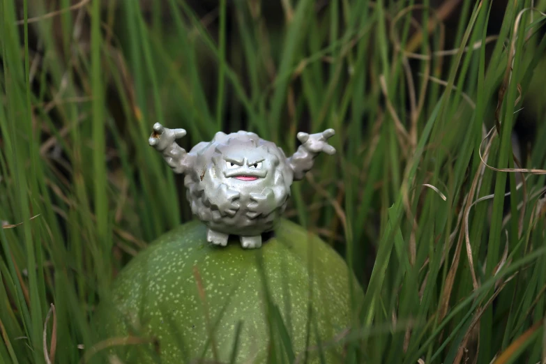 a figurine of a sheep sitting on top of a green ball, a macro photograph, inspired by Studio Ghibli, happening, gengar, in the high grass, scary angry pose, made out of shiny white metal