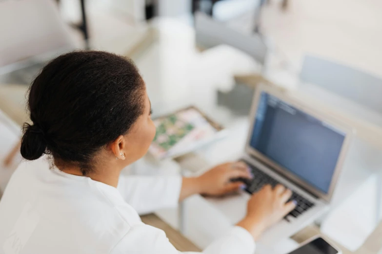 a woman sitting at a desk using a laptop computer, trending on pexels, wearing a white lab coat, afro tech, bottom angle, thumbnail