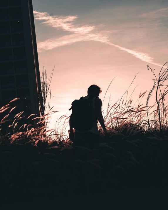 a person standing on top of a grass covered field, ((sunset)), with a backpack, wandering in the city, photography )