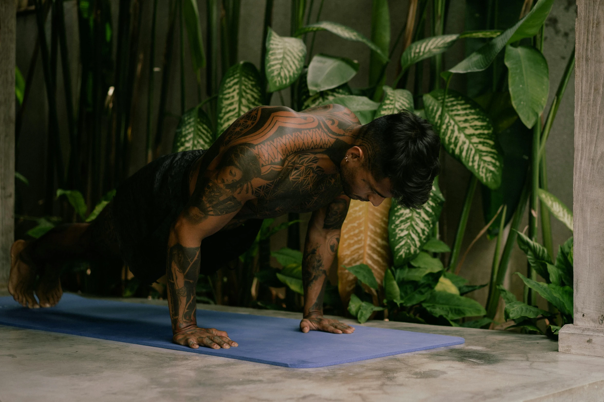 a man doing a yoga pose on a blue mat, a tattoo, covered in plants, keng lye, musculated, upper body image