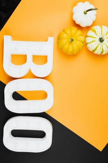 the word boo spelled in plastic letters next to pumpkins and gourds, by Julia Pishtar, geometric backdrop; led, on a yellow canva, mid view, black and white only