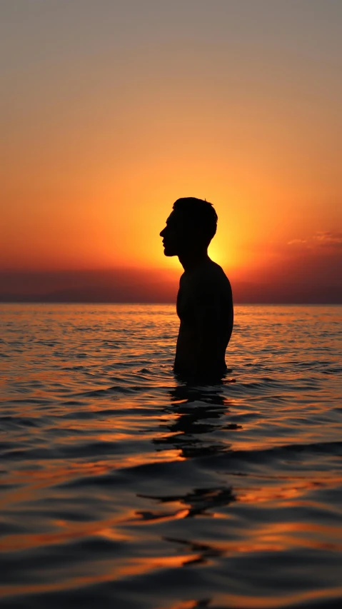 a man standing in the ocean at sunset, an album cover, by Alexis Grimou, pexels, lgbtq, young greek man, silhouette :7, peaceful face