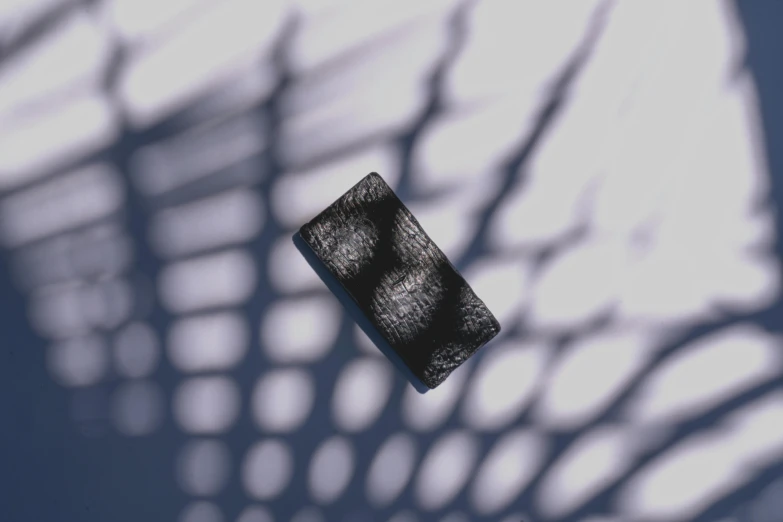 a cell phone sitting on top of a table, a stipple, inspired by Anna Füssli, unsplash, generative art, volumetric shadow, lattice, fur simulation, black 3 d cuboid device