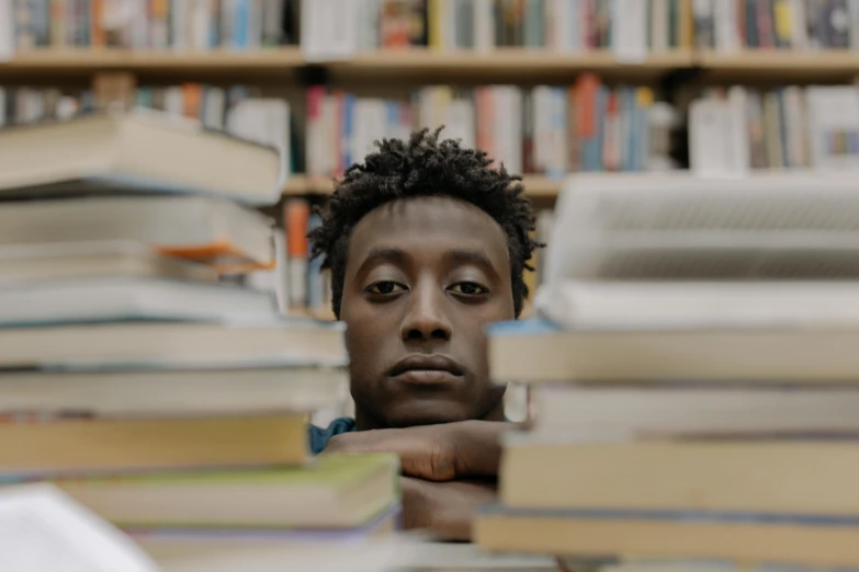 a man sitting in front of a pile of books, a portrait, by Matija Jama, pexels contest winner, lil uzi vert, centered face shot, still frame from a movie, student