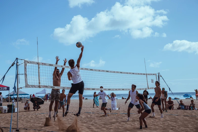 a group of young men playing volleyball on a sandy beach