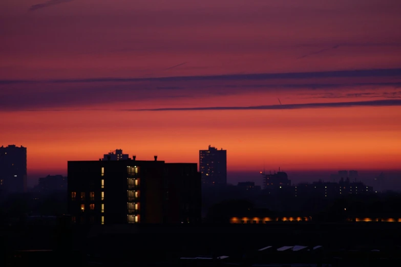 a very tall building sitting in the middle of a city, inspired by Elsa Bleda, pexels contest winner, brutalism, purple sunset, dark orange night sky, rooftop romantic, image from afar