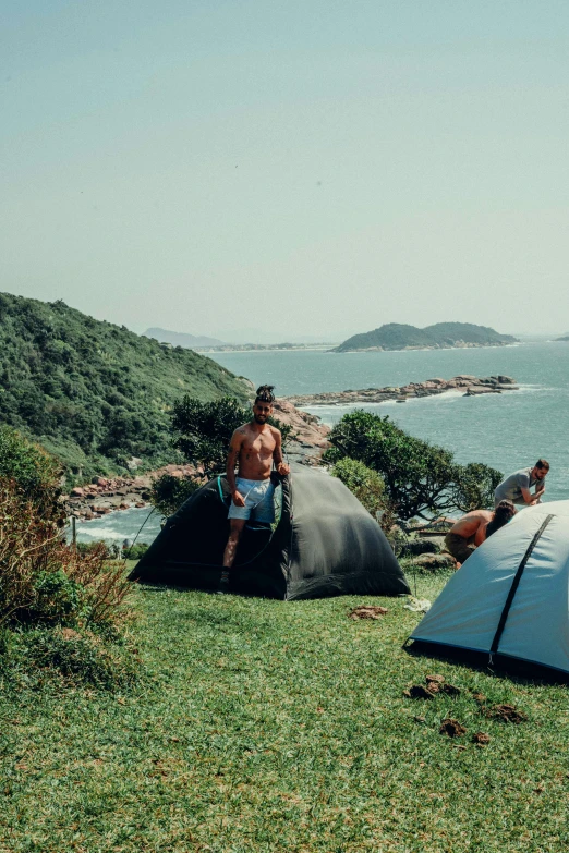 a couple of people sitting on top of a lush green hillside, tents, on the ocean, são paulo, profile image