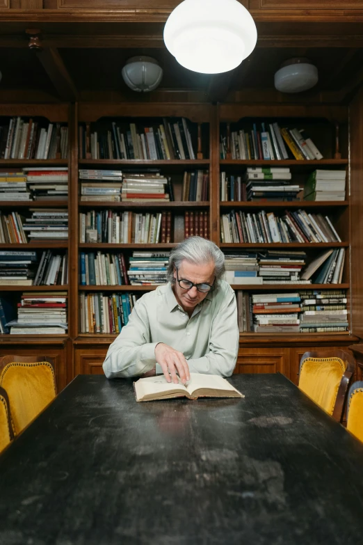 a man sitting at a table reading a book, by Carlo Randanini, pexels contest winner, modernism, a silver haired mad, annie liebovitz photography, librarian, david shing