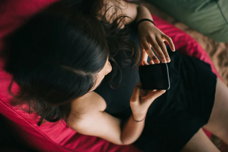 a woman laying on a bed using a cell phone, trending on pexels, wearing a cropped black tank top, avatar image, top down photo, girls