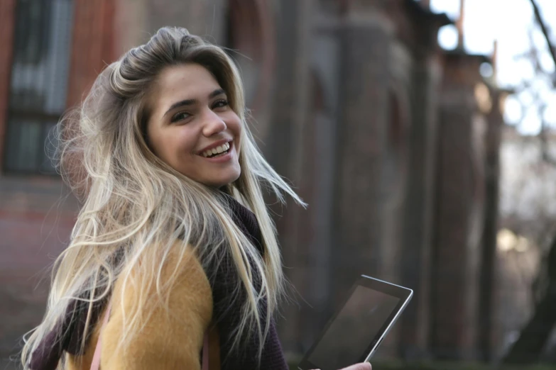 a woman smiles while holding a tablet computer, a photo, by Alice Mason, pexels contest winner, blonde beautiful young woman, anastasia ovchinnikova, looking to the right, cool tousled hair