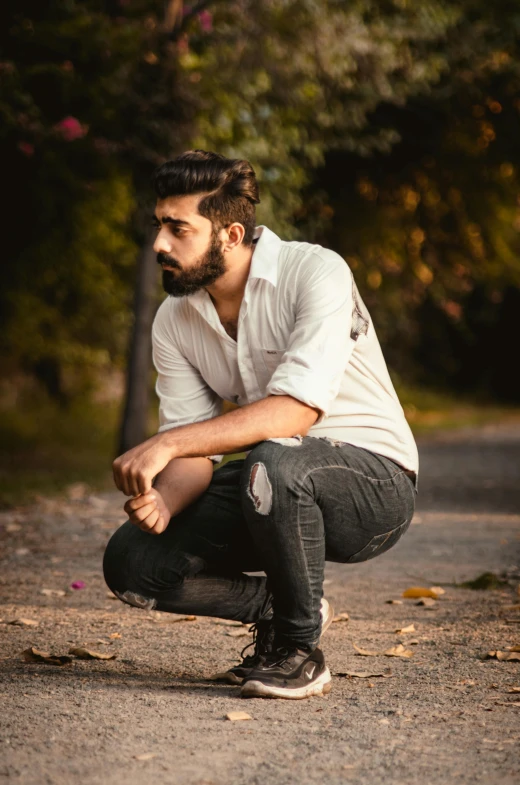 man crouching on the ground in front of trees