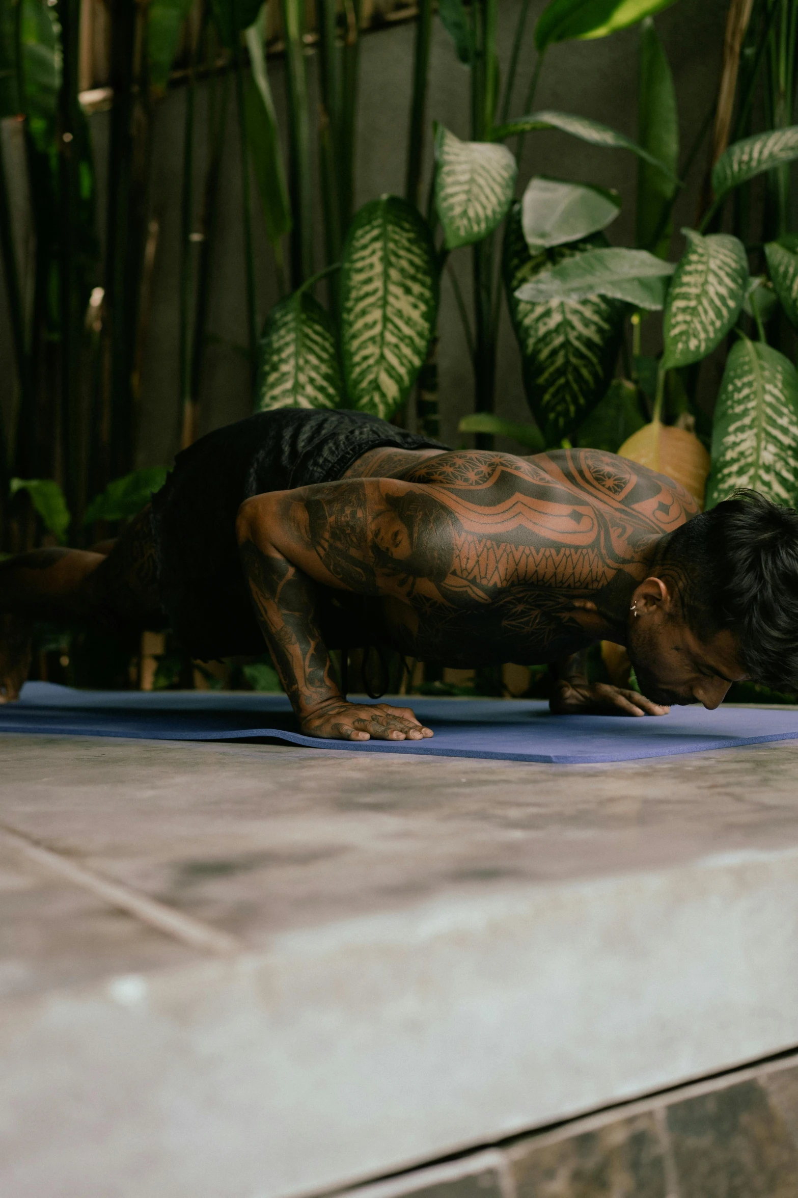 a man doing a yoga pose on a blue mat, a tattoo, covered in plants, malaysian, profile image, trending photo