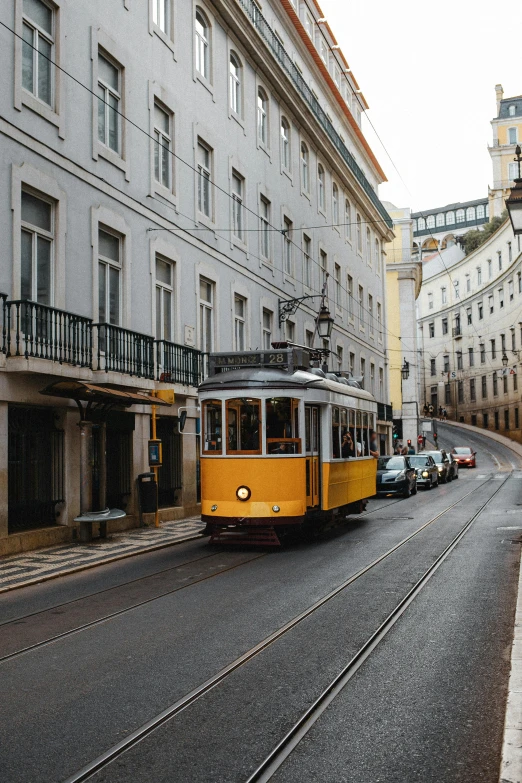 a yellow trolley traveling down a street next to tall buildings, pexels contest winner, viennese actionism, portugal, preserved historical, grey, brown