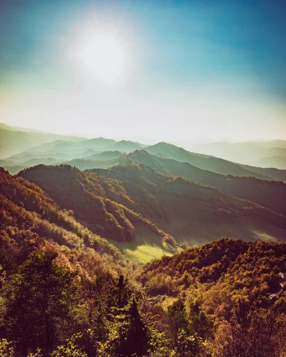 a mountain valley with trees and the sun above