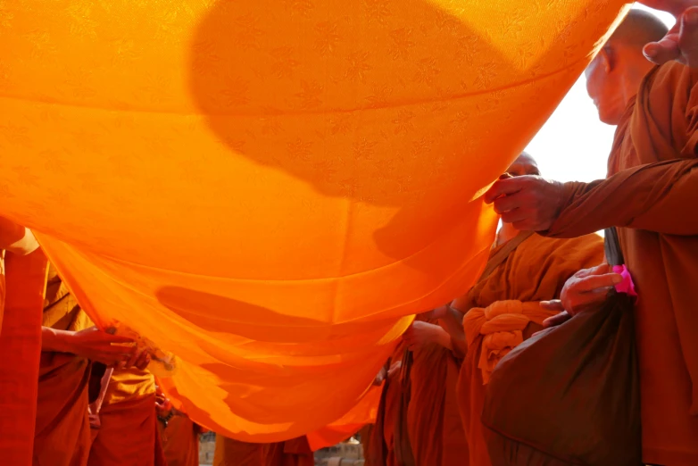 a group of monks standing next to each other, inspired by Christo, unsplash, process art, hanging from a hot air balloon, orange color, cambodia, overexposed sunlight