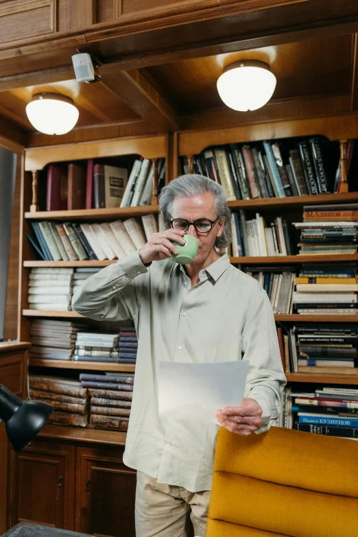 a man standing in front of a desk holding a piece of paper, drinking tea, dusty library, gray haired, full of greenish liquid