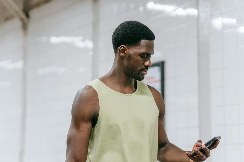 a man is looking at his cell phone, by Carey Morris, trending on pexels, pale green halter top, local gym, jaylen brown, background image