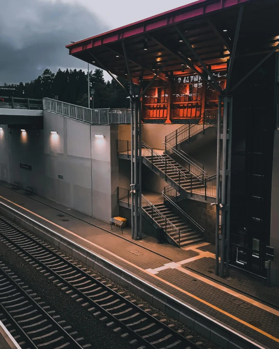 a train traveling down train tracks next to a train station, unsplash contest winner, regionalism, stairs, rain lit, photo of a big theaterstage, non-binary