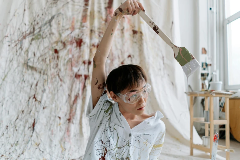 a woman sitting on the floor with a paintbrush in her hand, inspired by Pollock, pexels contest winner, action painting, young boy, raising an arm, wearing lab coat and glasses, mingchen shen