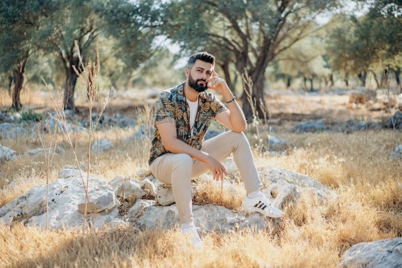 a man wearing all white sitting on a rock and looking off in the distance