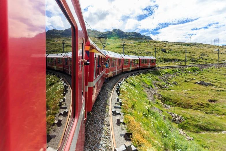 a red train traveling down train tracks next to a lush green hillside, by Werner Andermatt, 🚿🗝📝