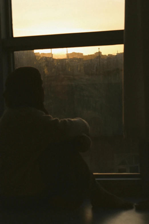 a person sitting at a table looking out a window, a picture, inspired by Elsa Bleda, pexels, realism, sundown, low quality photo, depressed, grainy footage