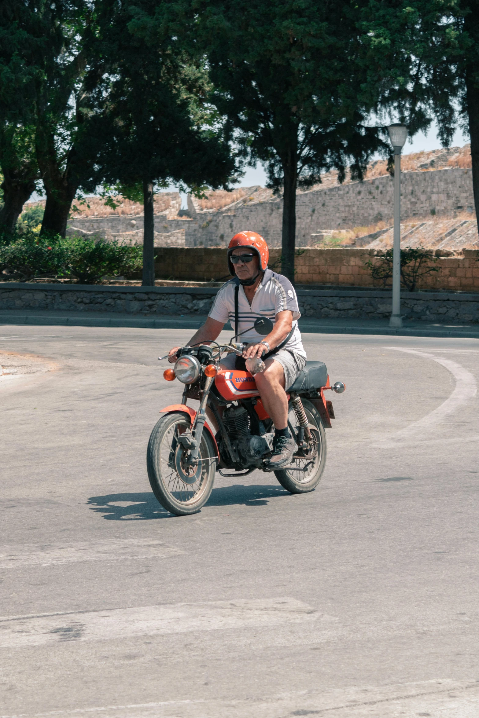 a man riding on the back of a motorcycle down a street, wearing orange sunglasses, at pamukkale, profile image, square