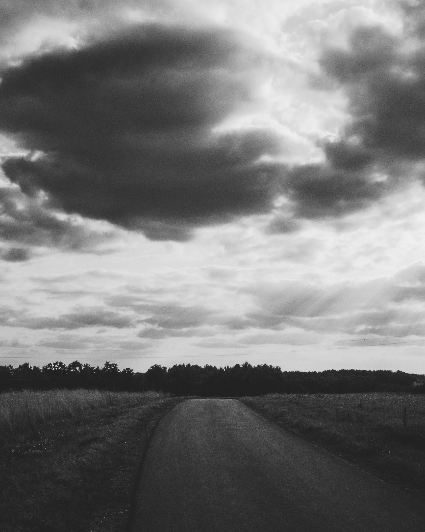 a cloudy sky over a country road in the middle of nowhere