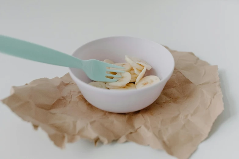 a bowl of food sitting on top of a piece of paper, by Emma Andijewska, trending on pexels, hurufiyya, banana color, using fork, celadon glaze, white backround